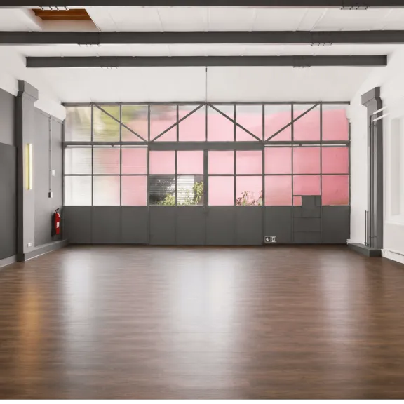 Leerer Raum mit Holzfußboden und großen Fenstern, rosa Licht von außen.