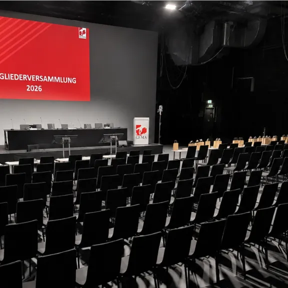 Leerer Konferenzsaal mit schwarzem Bestuhlung und roter Leinwand, Bühne vorne.