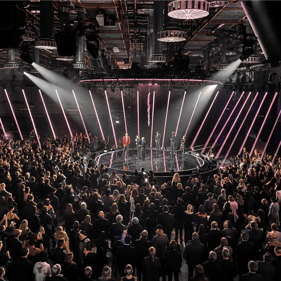Große Menschenmenge bei einer Bühnenshow mit Lichteffekten in einer Halle.