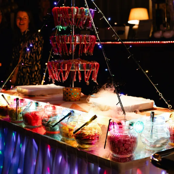 Bunte Süßigkeiten-Bar mit leuchtender Dekoration und verschiedenen Bonbongläsern.