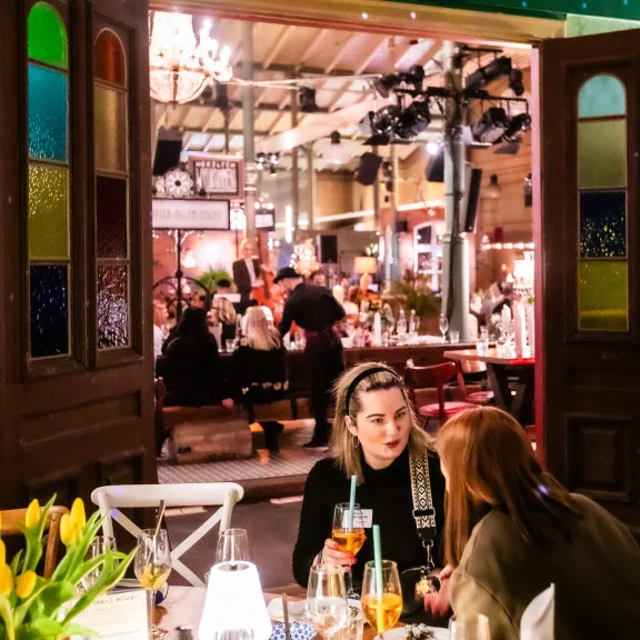 Zwei Frauen unterhalten sich an einem Tisch in einem bunt beleuchteten Restaurant.