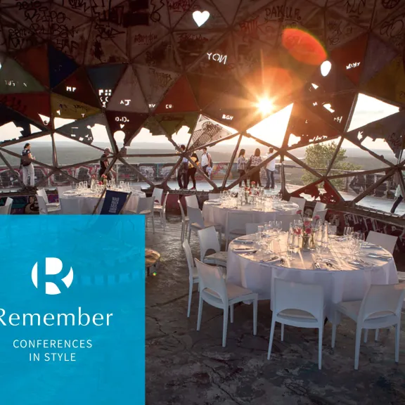 Gedeckte runde Tische mit weißen Stühlen unter Kuppel mit Sonnenuntergang im Hintergrund; im Vordergrund ein  blaues Quadrat mit weißen "R" und  und Text "Remember Conferences in Style"