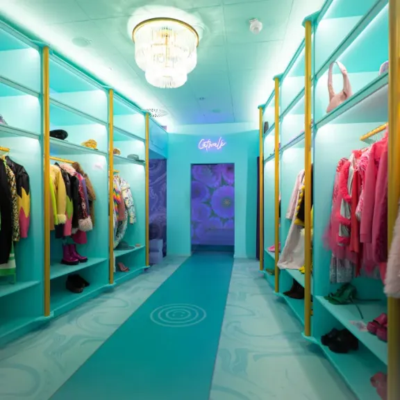 Großer, heller begehbarer Kleiderschrank mit bunten Kleidungsstücken und Kronleuchter.