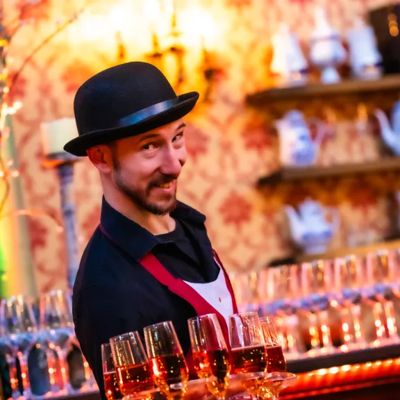 Kellner mit Bowlerhut trägt Tablett mit Sektgläsern in stilvoll dekorierter Bar.