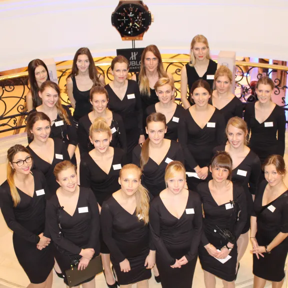 Gruppe junger Frauen in schwarzen Kleidern auf einer Treppe, alle schauen in die Kamera.