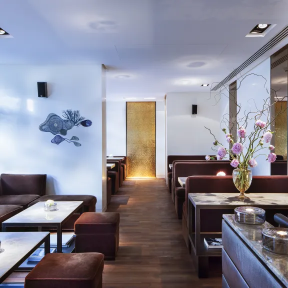 Modernes Café mit braunen Sofas, weißen Tischen und Blumenarrangement auf einer Kommode.