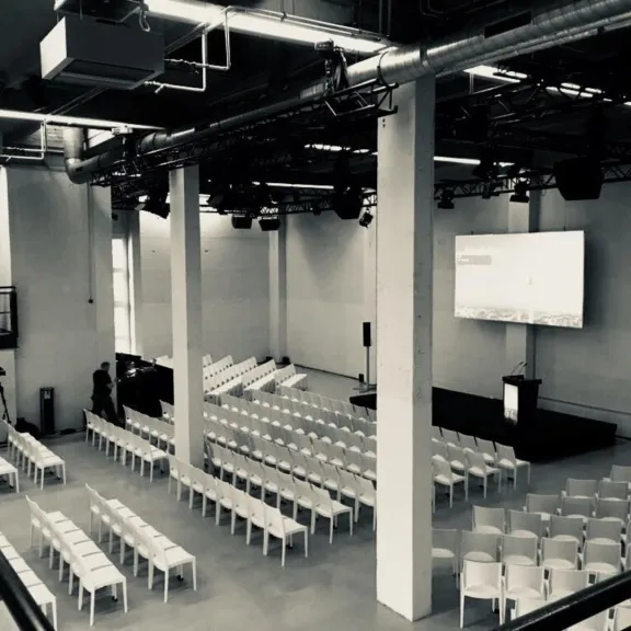Leerer Konferenzraum mit weißen Stühlen und großer Leinwand vorne.