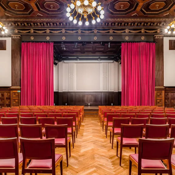 Theaterraum mit roten Stühlen, rotem Vorhang und verziertem Holzdach.