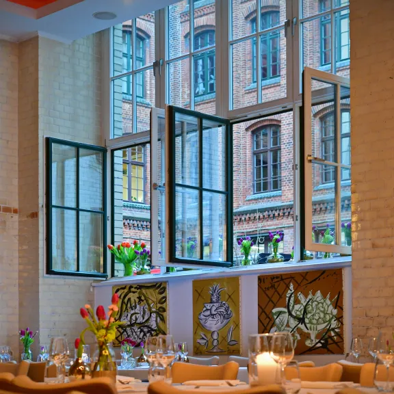 Restaurant mit großen offenen Fenstern, gedeckten Tischen und Blumenvasen.