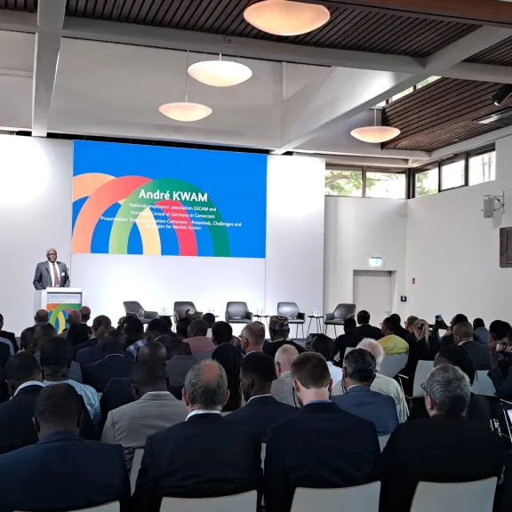 Mann spricht bei Konferenz vor großem Publikum, bunte Präsentation im Hintergrund.