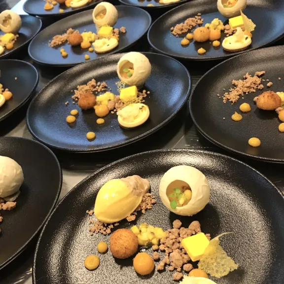Mehrere schwarze Teller mit kunstvoll angerichteten Dessertvariationen.