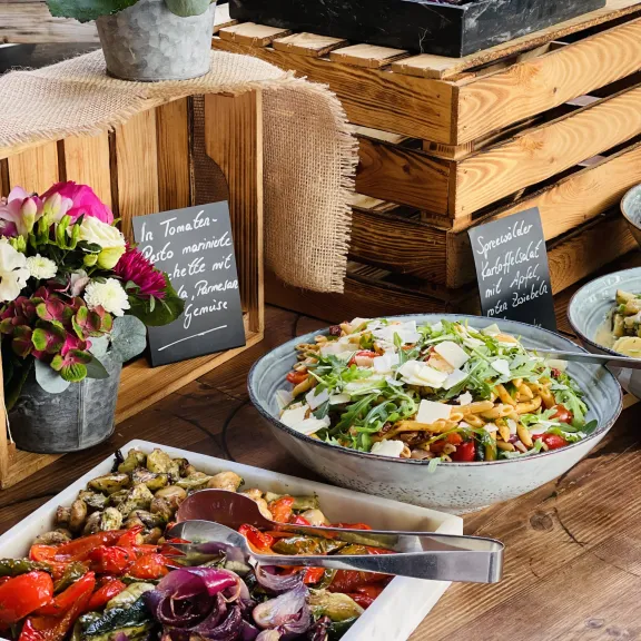 Buffet mit bunten Salaten, Gemüse und Blumen auf Holzplatten dekoriert.