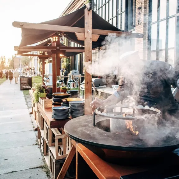 Koch auf Straßenmarkt grillt an großem Grill, viel Rauch steigt auf