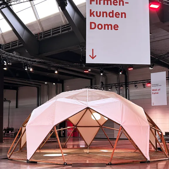 Große Messehalle mit futuristisch aussehender Kuppelstruktur aus Holz und Stoff.