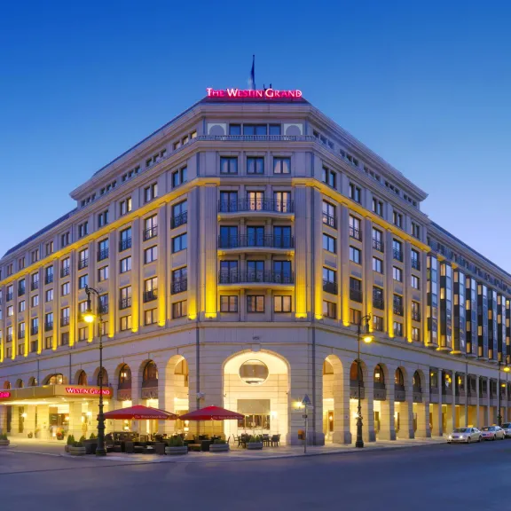 Großes, beleuchtetes Hotelgebäude an einer Straßenkreuzung bei Abenddämmerung.