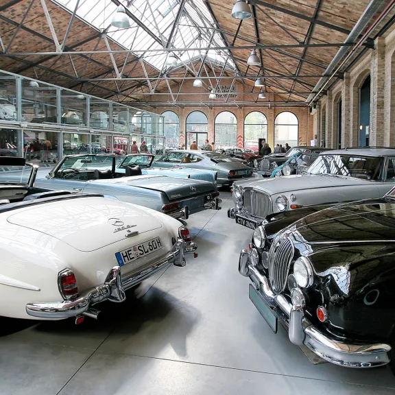 Klassische Oldtimer stehen in einer hellen, historischen Ausstellungshalle.