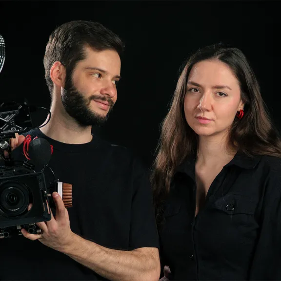 Zwei Personen im Fotostudio, einer hält eine Kamera, beide tragen schwarze Kleidung.