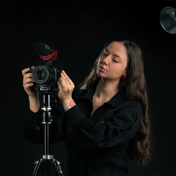 Frau mit langer brauner Haare richtet eine Kamera im Fotostudio ein.