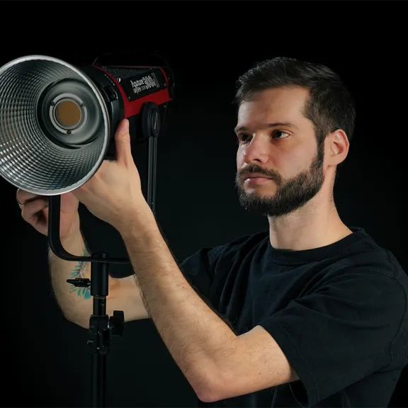 Mann stellt Studiolicht mit Reflektor vor schwarzem Hintergrund ein.