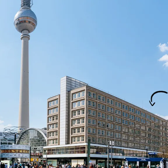 Berliner Fernsehturm und Gebäude am Alexanderplatz bei blauem Himmel mit weißen Wolken.