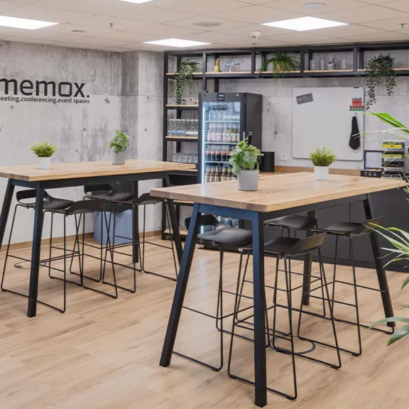 Moderne Büro-Küche mit hohen Tischen, Stühlen und vielen grünen Pflanzen.
