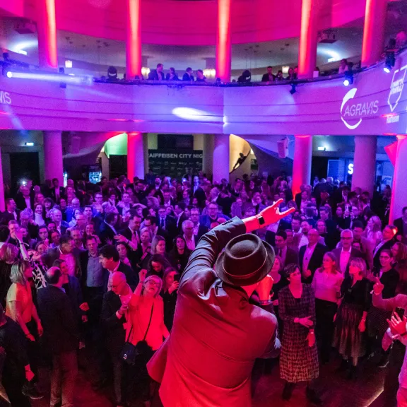 Menschenmenge auf einer Party mit bunter Beleuchtung und Musiker auf der Bühne.