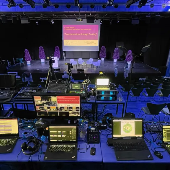Regieraum mit Technik und Laptops vor einer leeren Bühne in einem Veranstaltungsraum