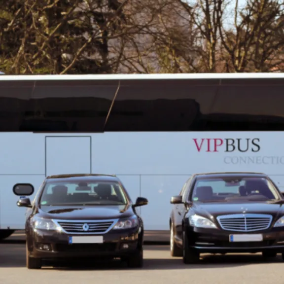 Mehrere schwarze Limousinen und ein großer VIP-Reisebus auf einem Parkplatz.