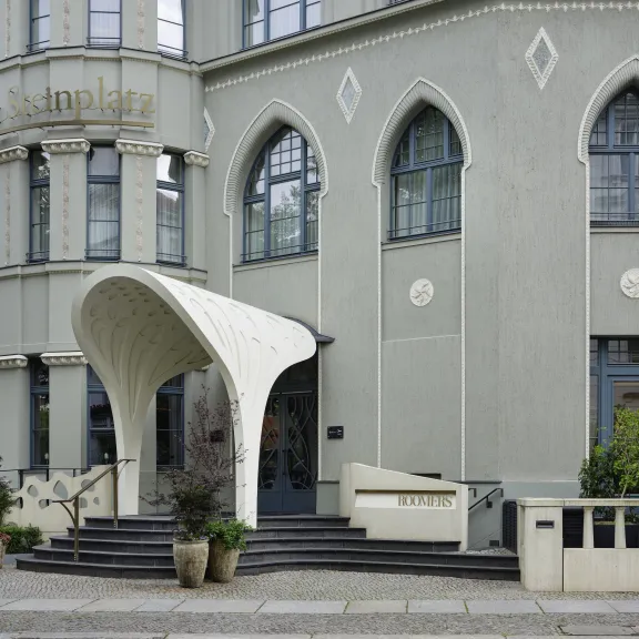 Hoteleingang mit modernem weißen Vordach, großen Fenstern und grauer Fassade