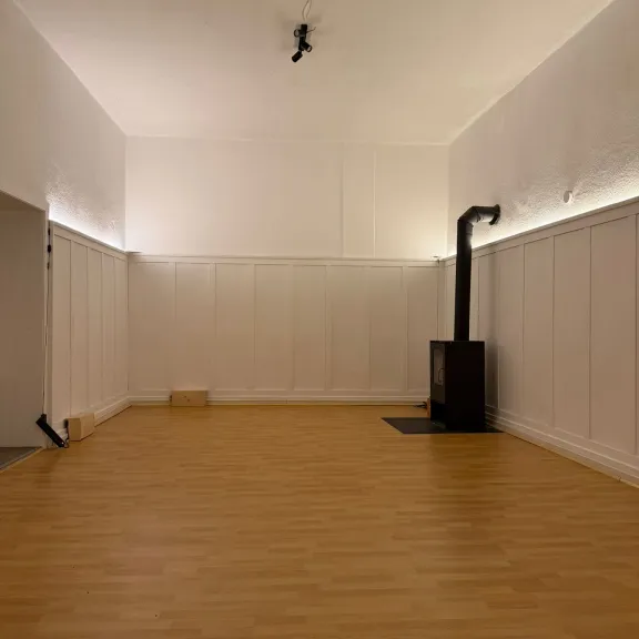 Leerer Raum mit hellem Holzfußboden und einem schwarzen Ofen in der Ecke
