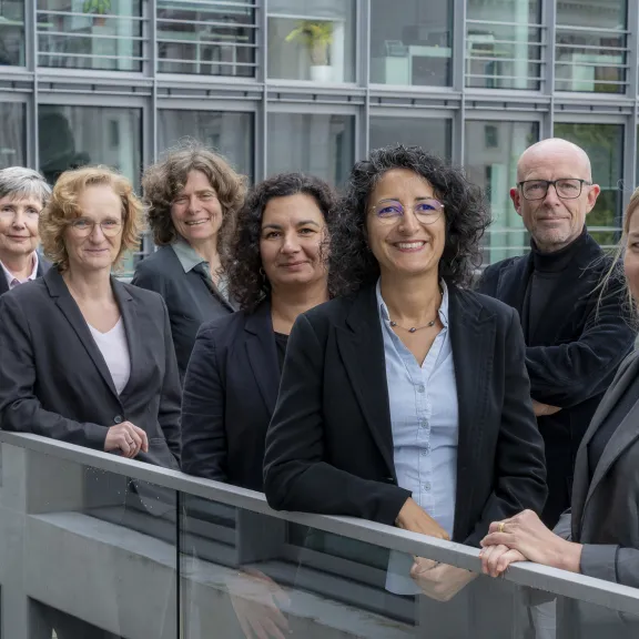 Neun Personen im Business-Outfit stehen lächelnd vor einem modernen Gebäude.