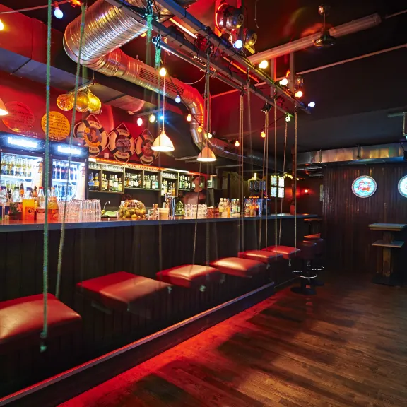 Leere Bar mit roten Hockern, bunter Beleuchtung und Zapfhähnen am Tresen.