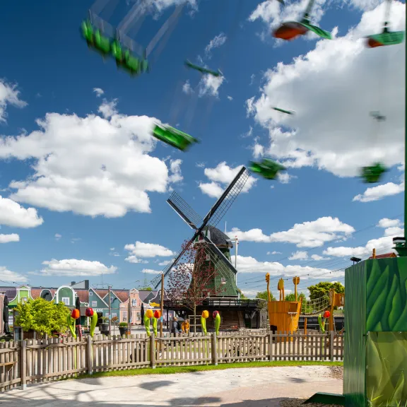 Windmühle im Freizeitpark bei sonnigem Wetter, Karussell im Vordergrund.