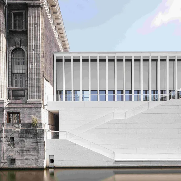 Altes Steingebäude neben modernem weißen Bau am Wasser.