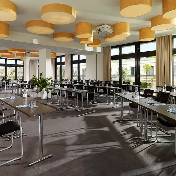 Heller Konferenzraum mit vielen Tischen, Stühlen und großen Fenstern
