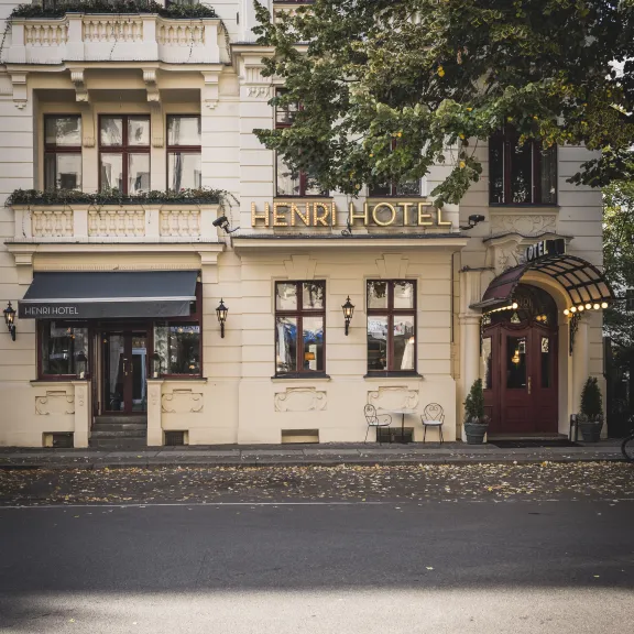 Helles Hotelgebäude mit rotem Eingang und goldener "Henri Hotel" Beschriftung.