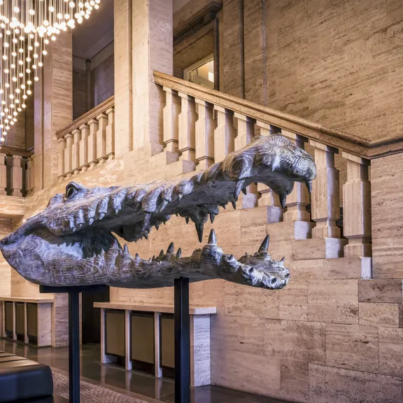 Krokodilschädel-Skulptur in einer eleganten Hotellobby mit Treppe und Lichterkette.