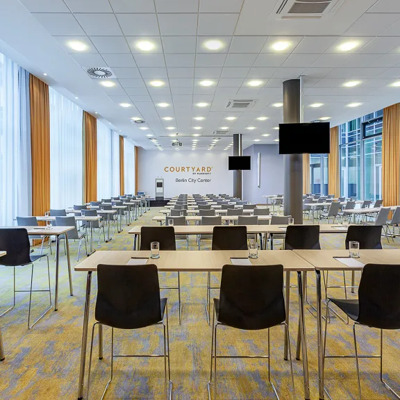 Moderner, heller Konferenzraum mit vielen leeren Tischen und Stühlen.