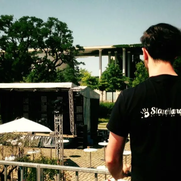 Mann mit schwarzem T-Shirt blickt auf eine leere Open-Air-Bühne im Park.
