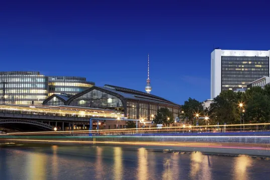 Berliner Stadtansicht bei Nacht mit beleuchteten Gebäuden und Fernsehturm im Hintergrund.