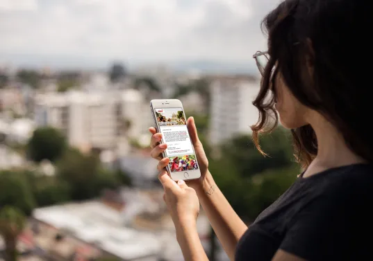 Frau mit Smartphone blickt auf Stadt im Hintergrund, Sommer, unscharfer Ausblick