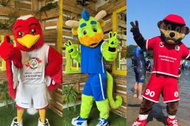 Drei bunte Maskottchen in Sportkleidung posieren fröhlich nebeneinander.
