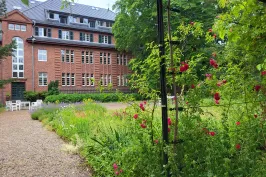 Rotes Backsteingebäude mit Garten, Blumen und Kletterrosen im Vordergrund.