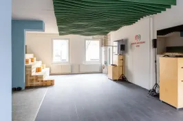 Heller Veranstaltungsraum mit großen Fenstern, modularer Holztribüne und flexibler Technik. An der Decke wellenförmige Elemente, an der Wand das Logo der Cradle to Cradle NGO. Offene Fläche für Workshops und Events.