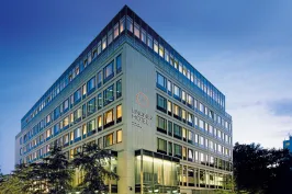 Modernes Hotelgebäude bei Dämmerung mit beleuchteten Fenstern und Bäumen davor.