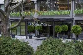Hoteleingang von DoubleTree mit Glasfassade und grünen Pflanzen in Töpfen.