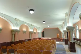 Leerer Saal mit Holzstühlen, gewölbten Decken und hellem Licht.