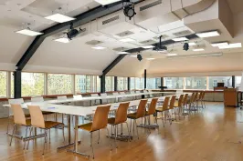 Moderner Konferenzraum mit langen Tischen, Holzstühlen und großen Fenstern