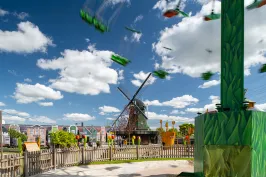 Windmühle im Freizeitpark bei sonnigem Wetter, Karussell im Vordergrund.