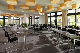 Heller Konferenzraum mit vielen Tischen, Stühlen und großen Fenstern